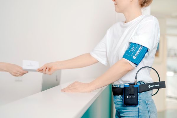 Patientin mit Langzeit-Blutdruckmessgerät an der Anmeldung der Herzpraxis Magdeburg beim Empfang.