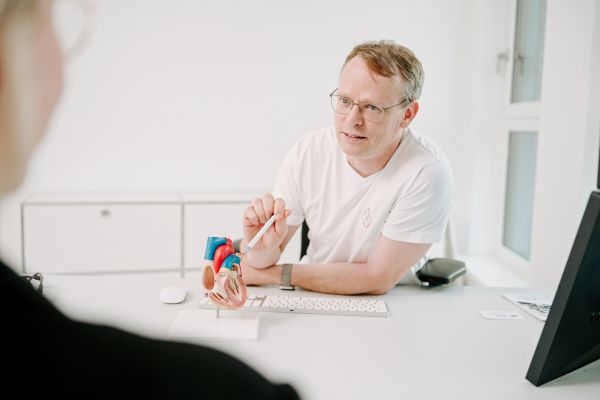 Arzt der Herzpraxis Magdeburg erklärt einer Patientin Herzerkrankungen anschaulich mit einem Herzmodell.