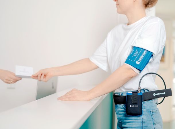 Patientin mit Langzeit-Blutdruckmessgerät an der Anmeldung der Herzpraxis Magdeburg beim Empfang.